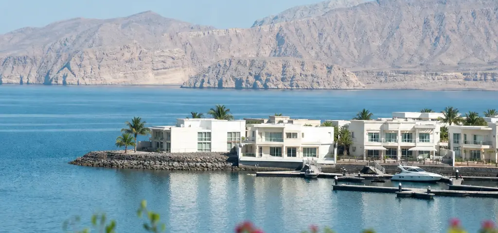 Aerial View Of A Muscat Waterfront Community With Marina, Villas And Mountains