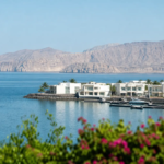 Aerial View Of A Muscat Waterfront Community With Marina, Villas And Mountains