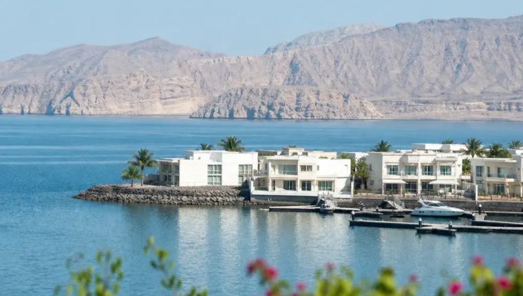 Aerial View Of A Muscat Waterfront Community With Marina, Villas And Mountains